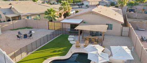 A residential backyard with a swimming pool, patio furniture, and a covered seating area.