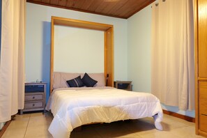 A bedroom with a bed, wooden headboard, nightstands, and a wooden door. - Charming 2-bedroom house on the Space Coast. (Melbourne)