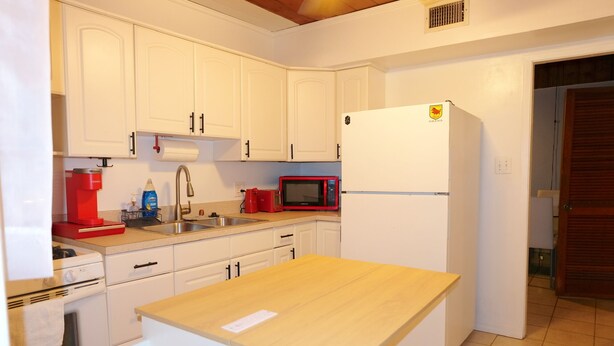 Eine Küche mit weißen Schränken, einem Holztisch, einer roten Mikrowelle, einem weißen Kühlschrank und einem Spülbecken.