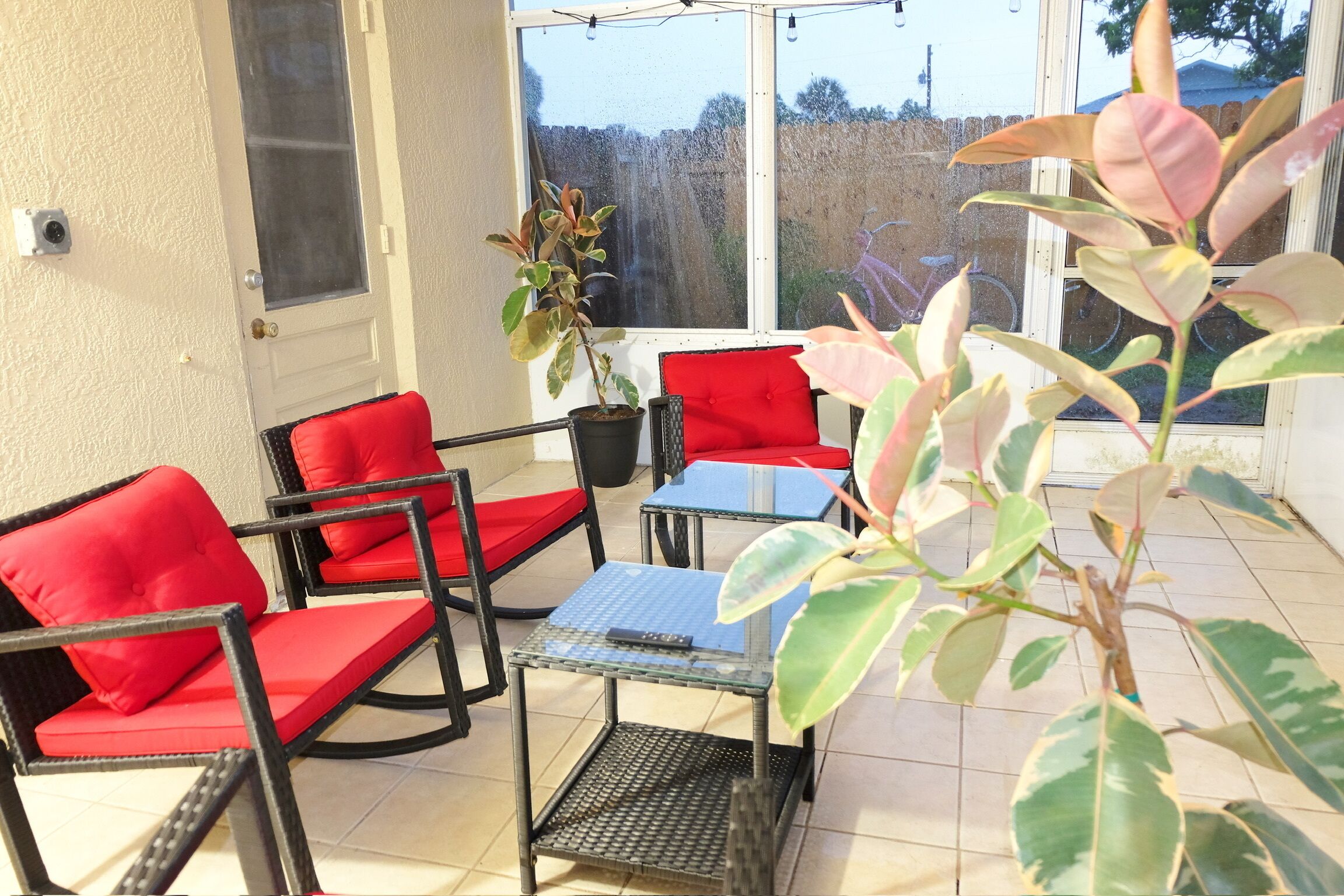 A sunlit patio with red cushioned chairs, a small table, and potted plants.