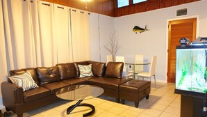 Ein Wohnzimmer mit einem braunen Ledersofa, einem Glastisch, einem Esstisch mit Stühlen und einem Aquarium.