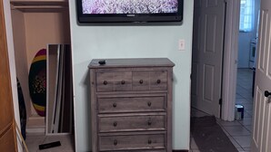 Ein Wohnzimmer mit an der Wand montiertem Fernseher, einer Holzkommode und einem Flur, der in einen anderen Raum führt.