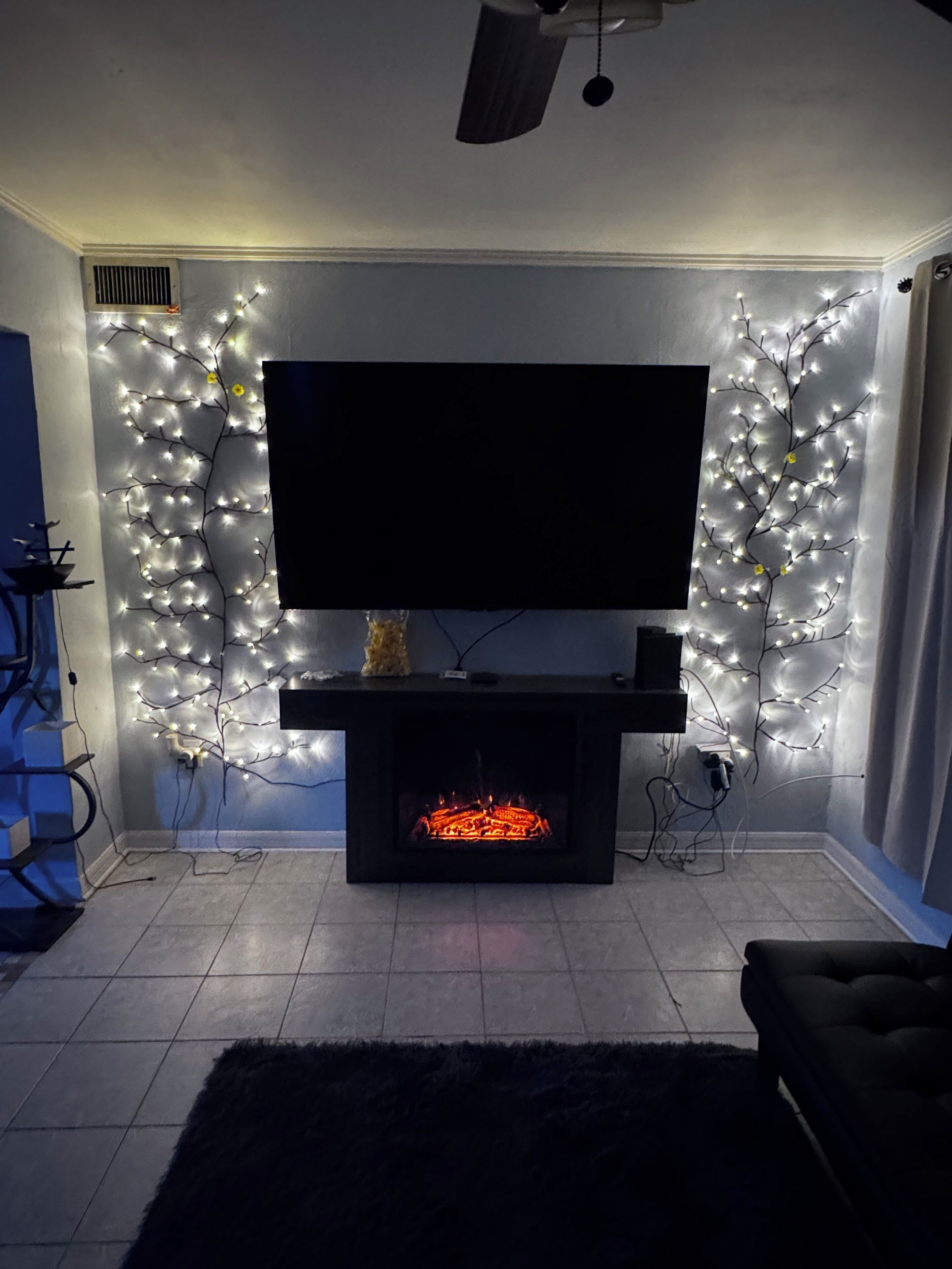 A living room with a flat-screen TV mounted on a black stand, a fireplace below, and decorative lights on the walls.