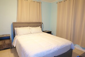 A bedroom with a bed, nightstands, and curtains. - Charming 2-bedroom house on the Space Coast. (Melbourne)