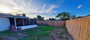 A backyard with a wooden fence, a covered patio area, and a clear sky. - Charming 2-bedroom house on the Space Coast. (Melbourne)