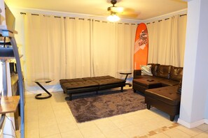 A living room with a sofa, a loveseat, a small table, a floor lamp, and a ceiling fan. - Charming 2-bedroom house on the Space Coast. (Melbourne)