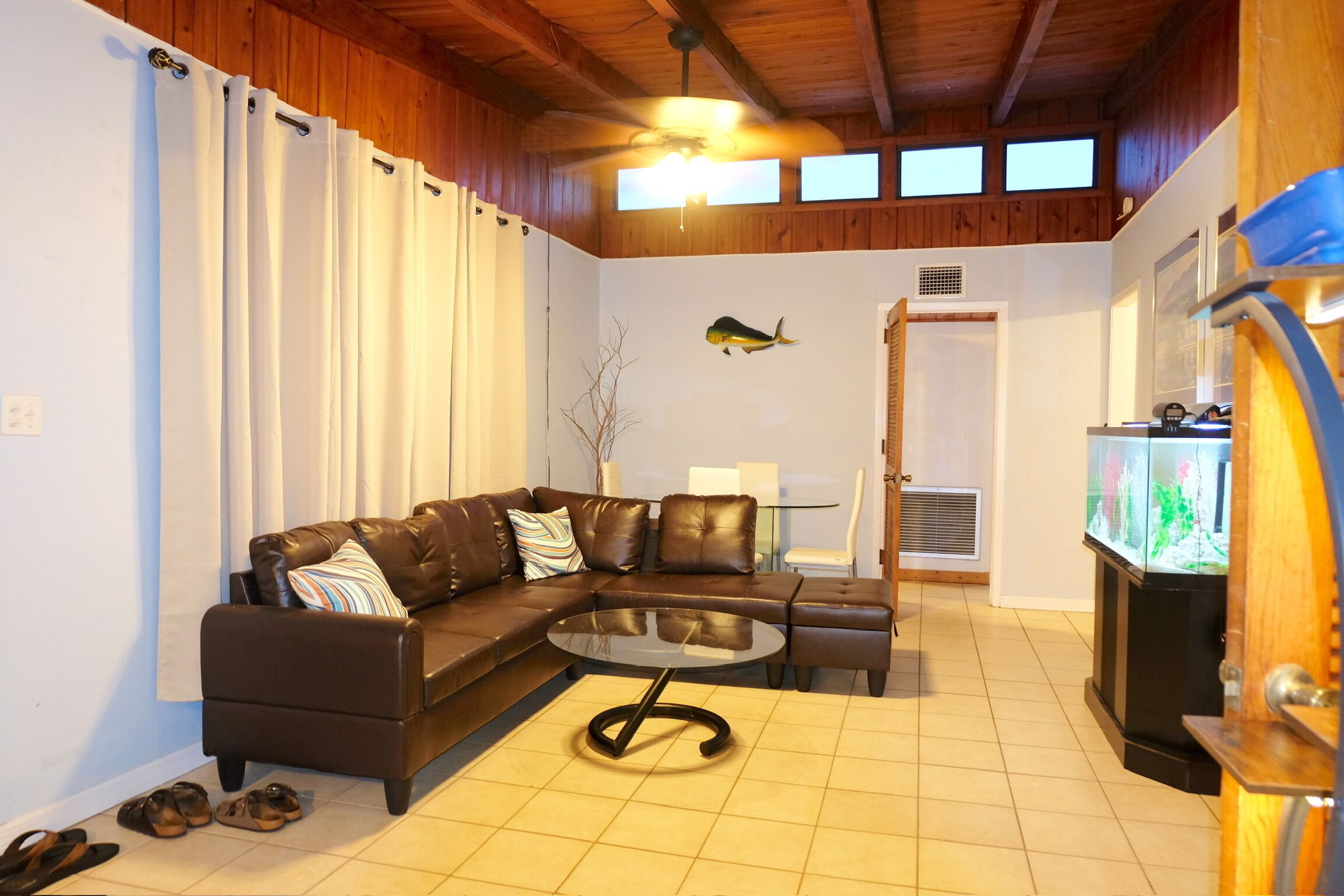A living room with a brown leather sofa, a glass coffee table, and a fish tank.