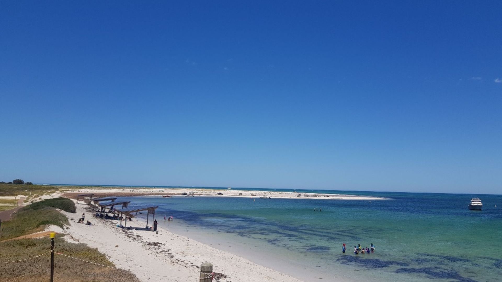 Een strand met helderblauw water, een zandstrand en enkele mensen in de verte.