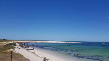 Een strand met helderblauw water, een zandstrand en enkele mensen in de verte.