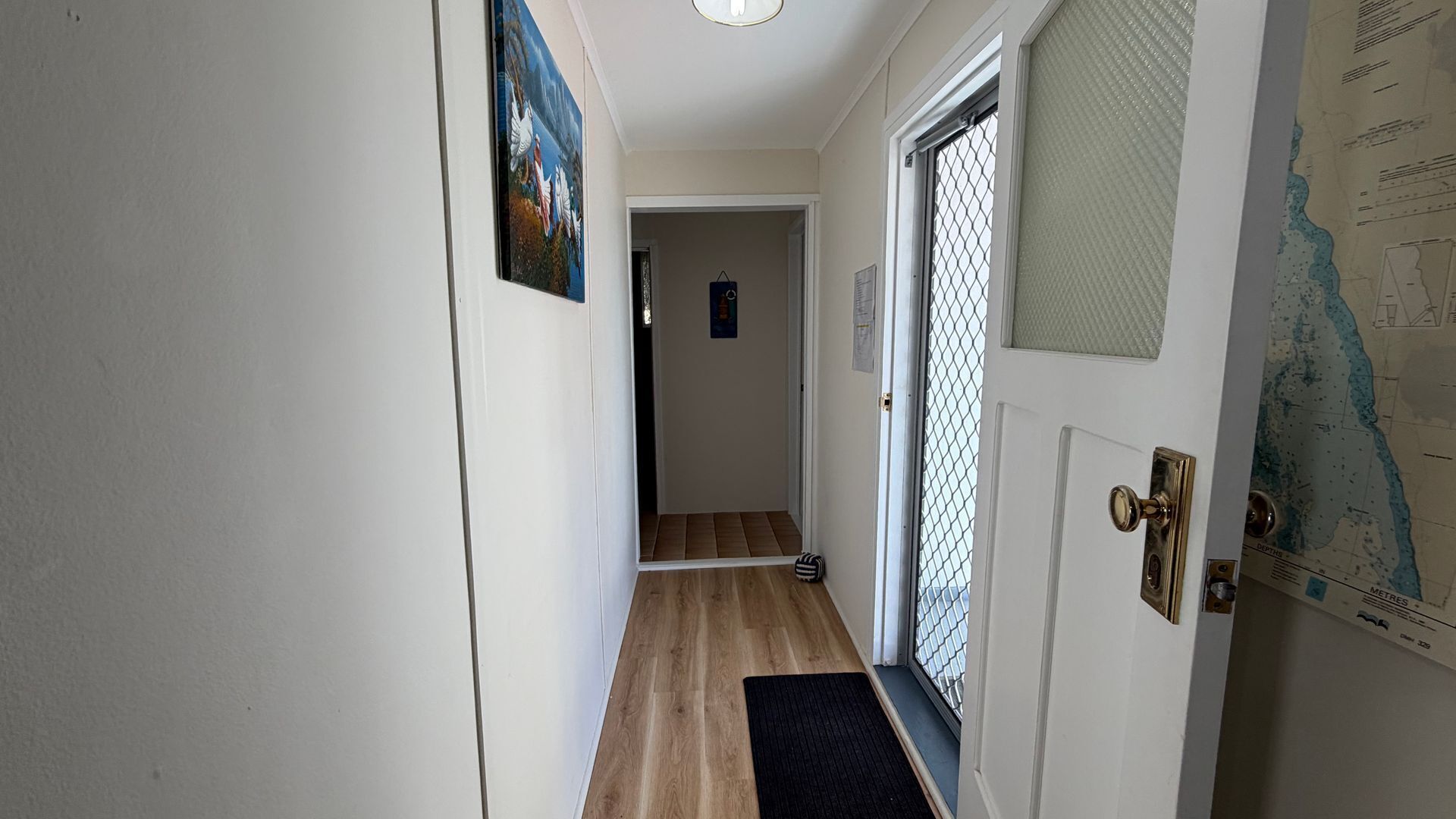 A hallway with a wooden floor, a door with a metal gate, and a wall with a map.