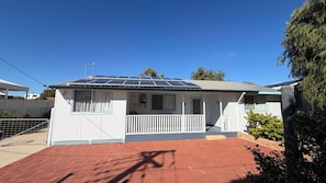 A single-story house with a solar panel roof, a fenced yard, and a red brick driveway.