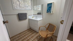A small bathroom with a white sink, a mirror, a towel, and a wicker chair.