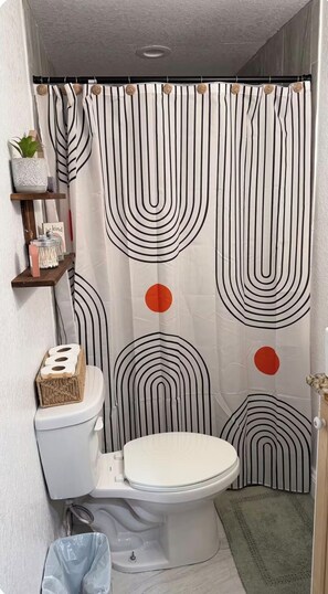 Ein Badezimmer mit gestreiftem Duschvorhang, Toilette, einem kleinen Ablagefach mit Gegenständen und einem grünen Teppich.
