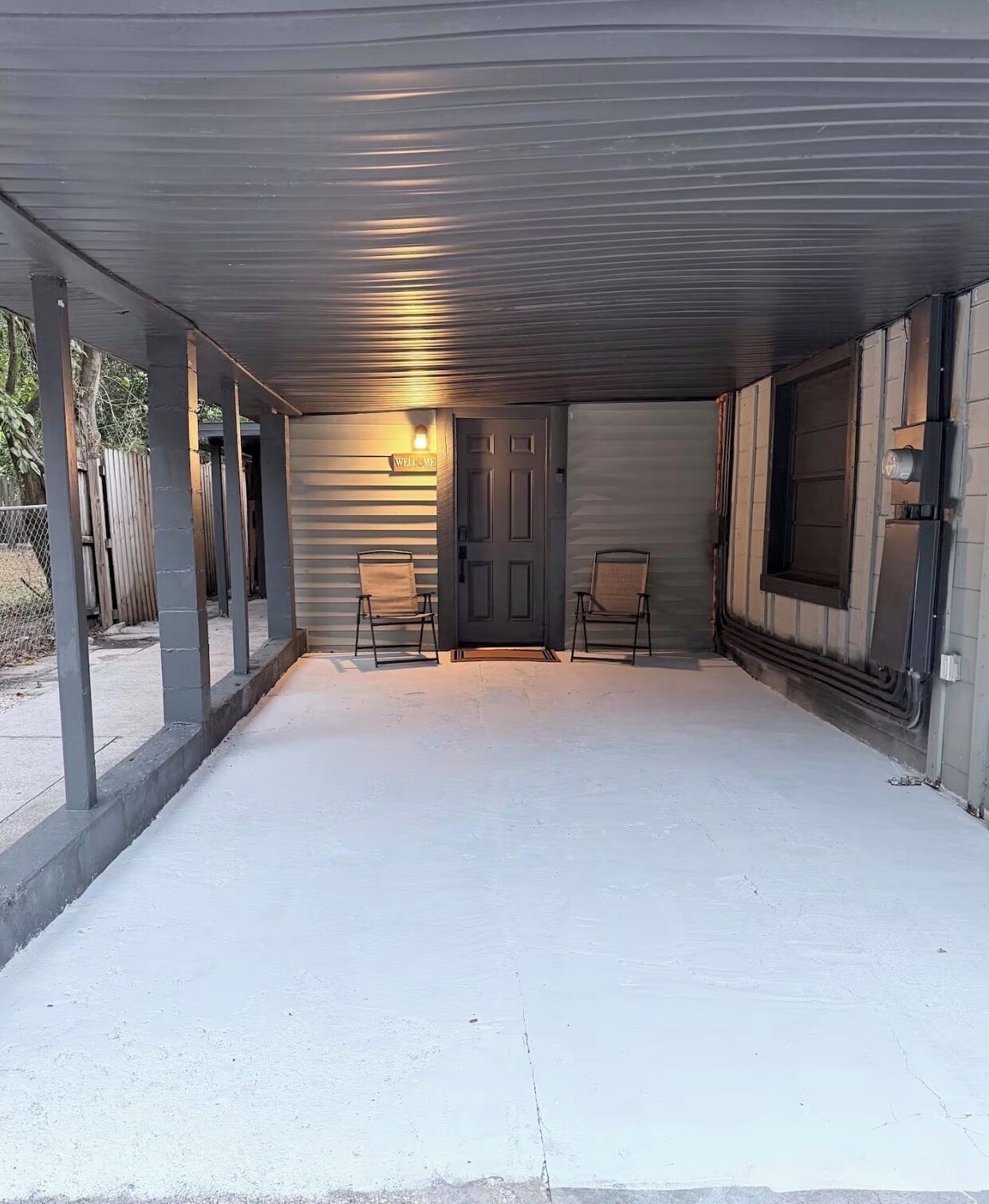 Un garage fermé avec un sol en béton, deux chaises, une porte et une pancarte indiquant « BIENVENUE ».