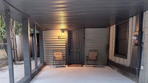 Uma garagem coberta com piso de concreto, duas cadeiras, uma porta e um letreiro com a palavra 'WELCOME'.