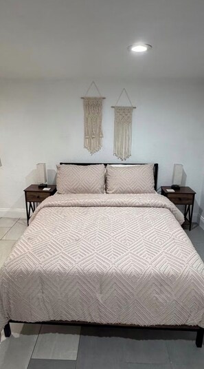 Ein Schlafzimmer mit einem Bett, zwei Nachttischen, zwei Wandbehängen aus Makramee und einer Deckenleuchte.