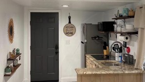 Uma cozinha com uma porta escura, uma placa na parede, bancada com banquetas e uma geladeira.