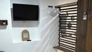 Quarto com cama, televisão na parede, portão de madeira e uma pequena prateleira com uma placa.