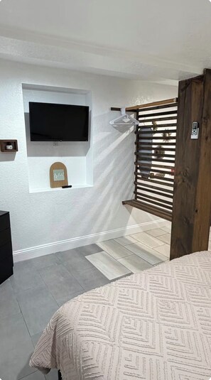 Ein Schlafzimmer mit einem Bett, einem an der Wand befestigten Fernseher, einem hölzernen Tor und einer kleinen Ablage mit einem Schild.