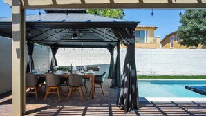 Un espacio de comedor al aire libre techado, con piscina, suelo de ladrillo y una estructura de pérgola.