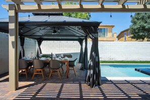 Ein überdachter Essbereich im Freien mit Pool, Backsteinböden und einer Pergola.