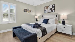 Un dormitorio con cama, mesitas de noche, un banco, ventilador de techo y obras de arte en la pared.