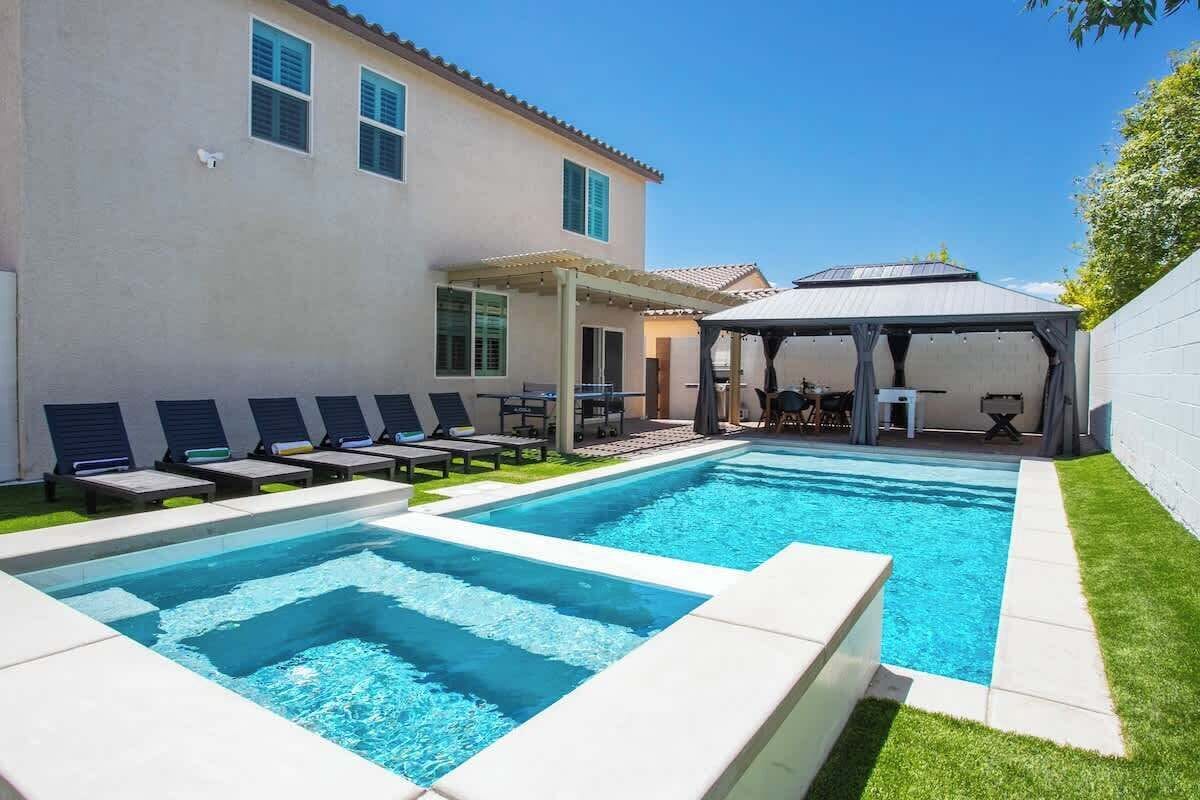 A swimming pool with lounge chairs, a covered patio, and a building with windows.