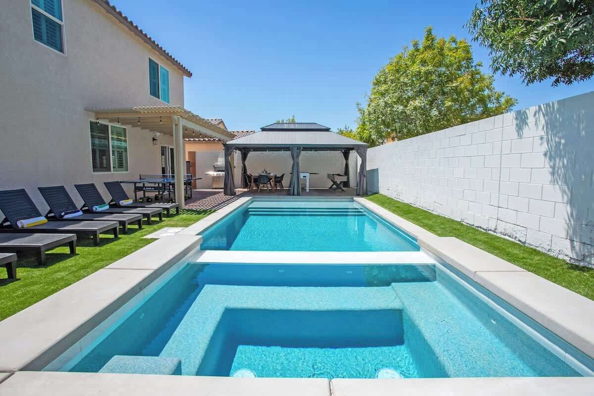 A rectangular swimming pool with a covered seating area and lounge chairs.