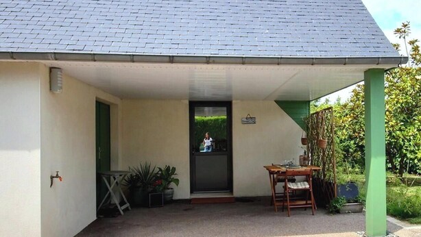 Zona exterior coberta amb taula i caires, una porta i un jardí petit.