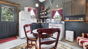 A kitchen with a refrigerator, stove, microwave, and a wooden chair. - The Stargazer Cabin - A Hill Country Retreat (Fredericksburg)