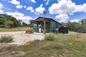 A rustic building with a weather vane, a door, and a small porch. - The Stargazer Cabin - A Hill Country Retreat (Fredericksburg)