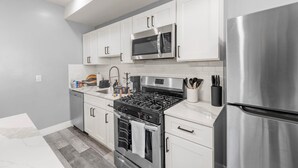 Una cocina moderna con armarios blancos, electrodomésticos de acero inoxidable y un salpicadero de azulejos grises.