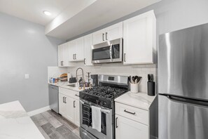 A modern kitchen with white cabinets, stainless steel appliances, and a grey tiled backsplash. - Modern 2BR Retreat • Free Parking • Near Philly Zoo (Philadelphia)