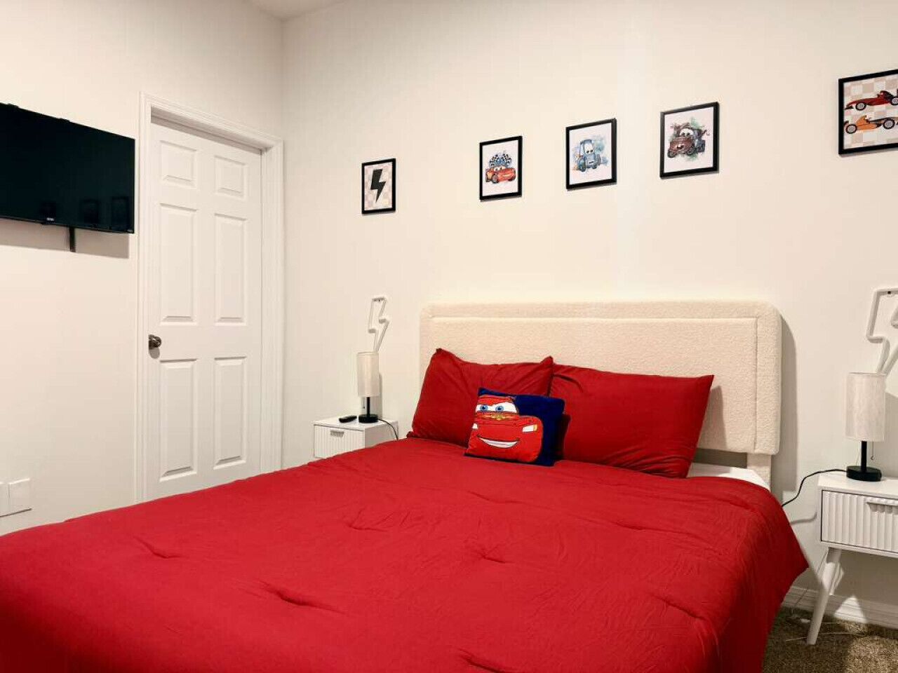 Une chambre avec une couvre-lit rouge, une porte blanche et quatre tableaux encadrés accrochés au mur.