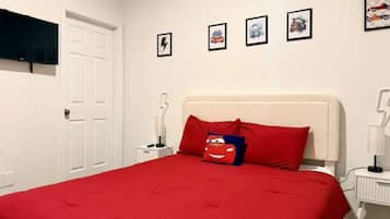 A bedroom with a red bedspread, a white door, and four framed pictures on the wall.