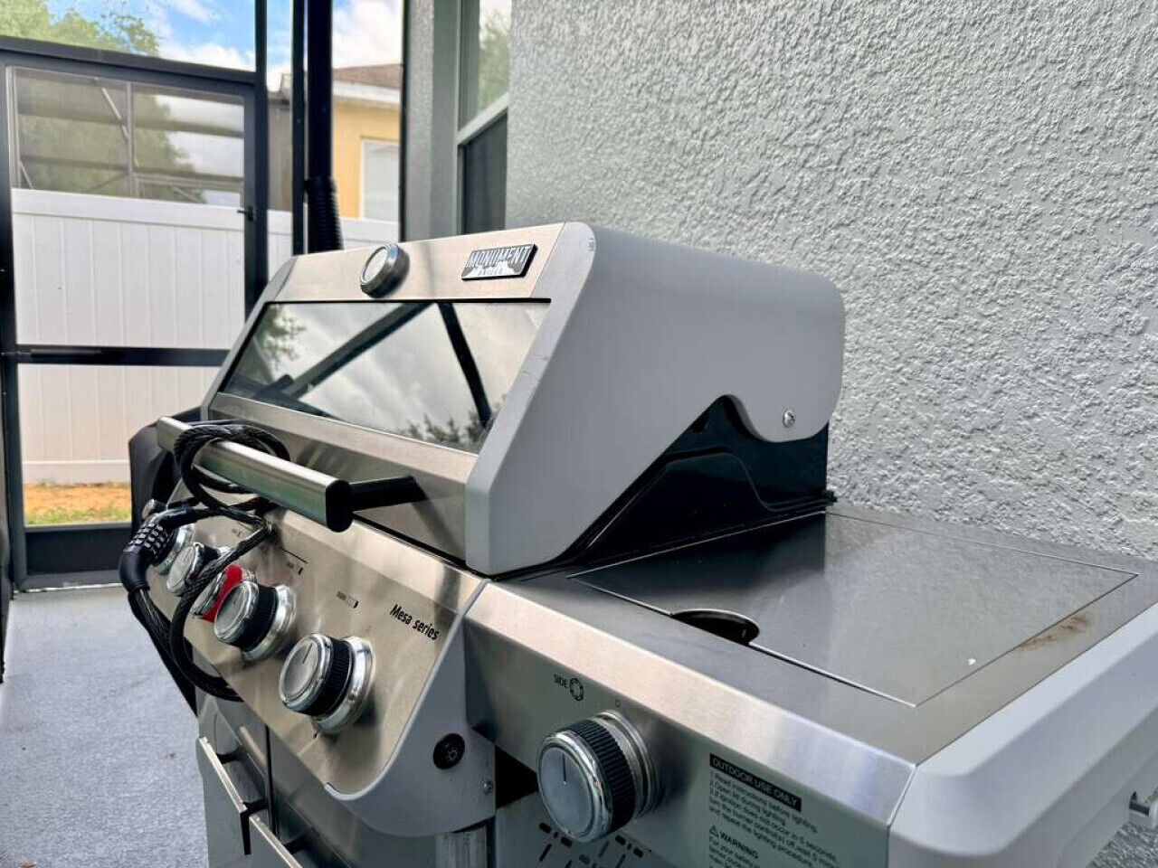 A portable gas grill with multiple burners and a digital display, placed outdoors against a textured wall.