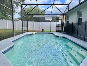 Ein Schwimmbecken mit überdachtem Bereich, umgeben von einem weißen Zaun und einem Haus im Hintergrund.