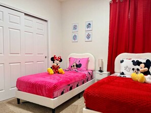 Ein Schlafzimmer mit zwei Betten, jedes mit Bettwäsche und Kuscheltieren im Mickey-Mouse-Design.