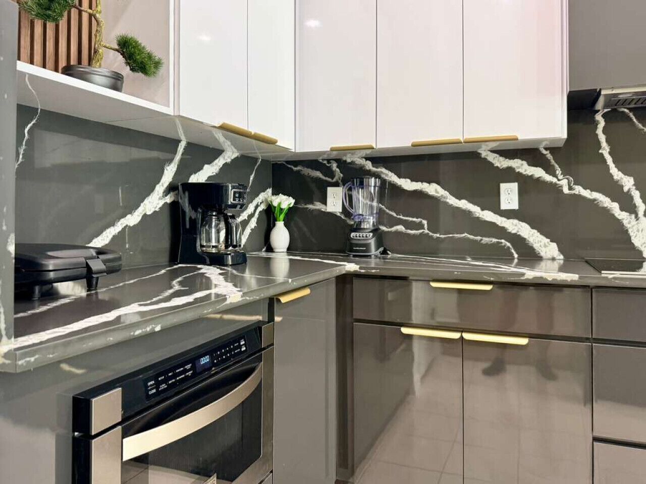 A modern kitchen with a marble backsplash, stainless steel appliances, and white cabinetry.