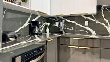 A modern kitchen with a marble backsplash, stainless steel appliances, and white cabinetry.