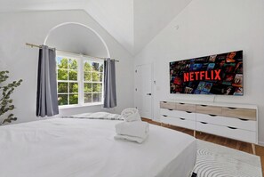 Habitación de hotel moderna con una cama grande, un televisor montado en la pared mostrando un diseño de Netflix y vistas a zonas verdes.
