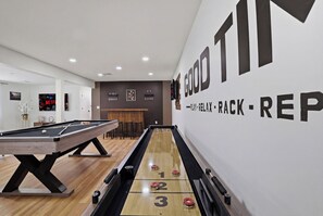 Ein Billardtisch und ein Shuffleboard-Tisch in einem Raum, dessen Wand die Aufschrift 'GOOD PLAY - RELAX - RACK - REP' trägt.