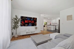 A modern living room with a large flat-screen TV displaying a Netflix interface, a sofa, a coffee table, and a potted plant. - NEW HOUSE • Hot Tub • Game Room • Fire Pit • Sleeps 12 • Near Lakes & Pools (Long Pond)