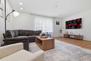 Ein modernes Wohnzimmer mit einer Eckcouch, einem Holztisch und einem großen Flachbildfernseher an der Wand.