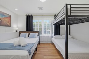 Ein Hotelzimmer mit Etagenbett, einem Einzelbett und einem großen Fenster mit Vorhängen.