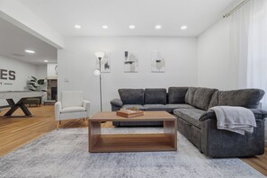 Ein modernes Wohnzimmer mit grauem Sofa, einem weißen Sessel und einem Holztisch.
