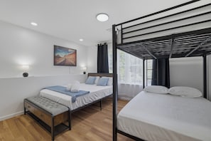 Ein Schlafzimmer mit Etagenbett, einem Einzelbett, einem Nachttisch mit Lampe, einem Fenster mit Vorhängen und einem Bild an der Wand.