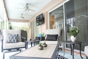 Ein überdachter Patio-Bereich mit zwei Stühlen, einem Tisch und einem an der Wand befestigten Fernseher.