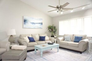 Ein Wohnzimmer mit zwei Sofas, einem Couchtisch, einer Lampe, einem Deckenventilator und einem großen Fenster.