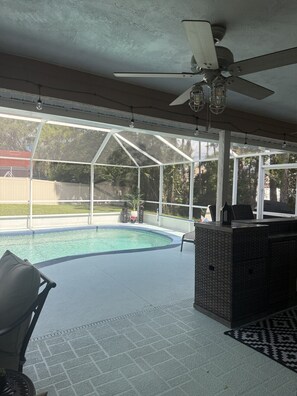 Ein überdachter Außenbereich mit Pool, Sitzgelegenheiten und Deckenventilator.